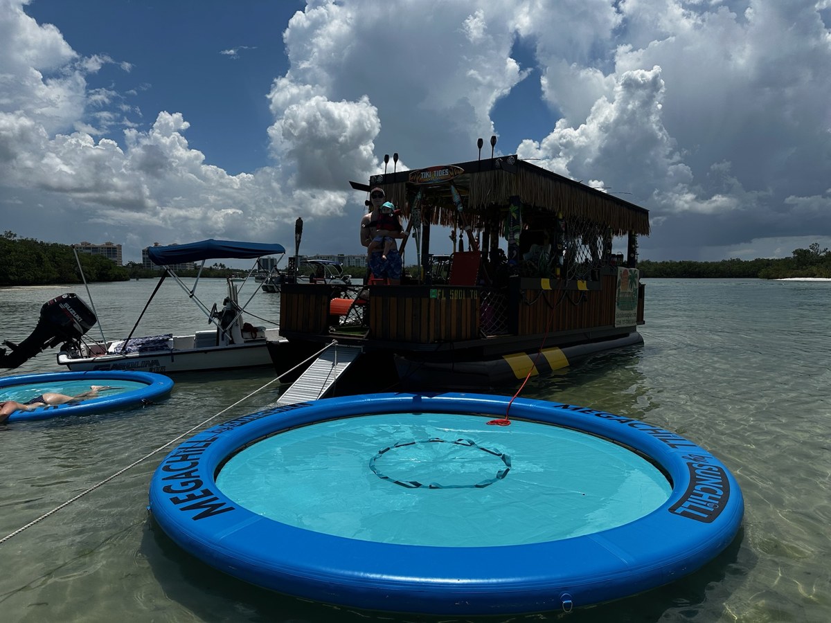 Tiki Tides boat anchored in shallow water with blue floating loungers and the boarding ramp deployed